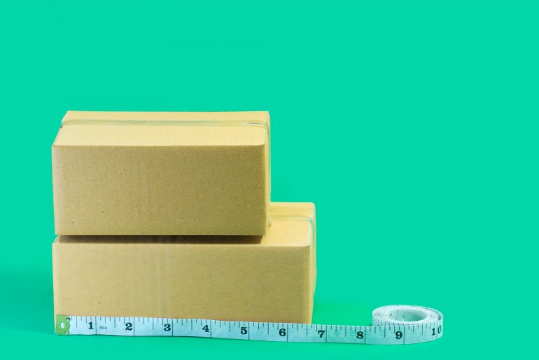 How is Dimensional Weight Calculated? The Complete Guide to Dimensional Shipping Cardboard boxes with tape measure on green background.